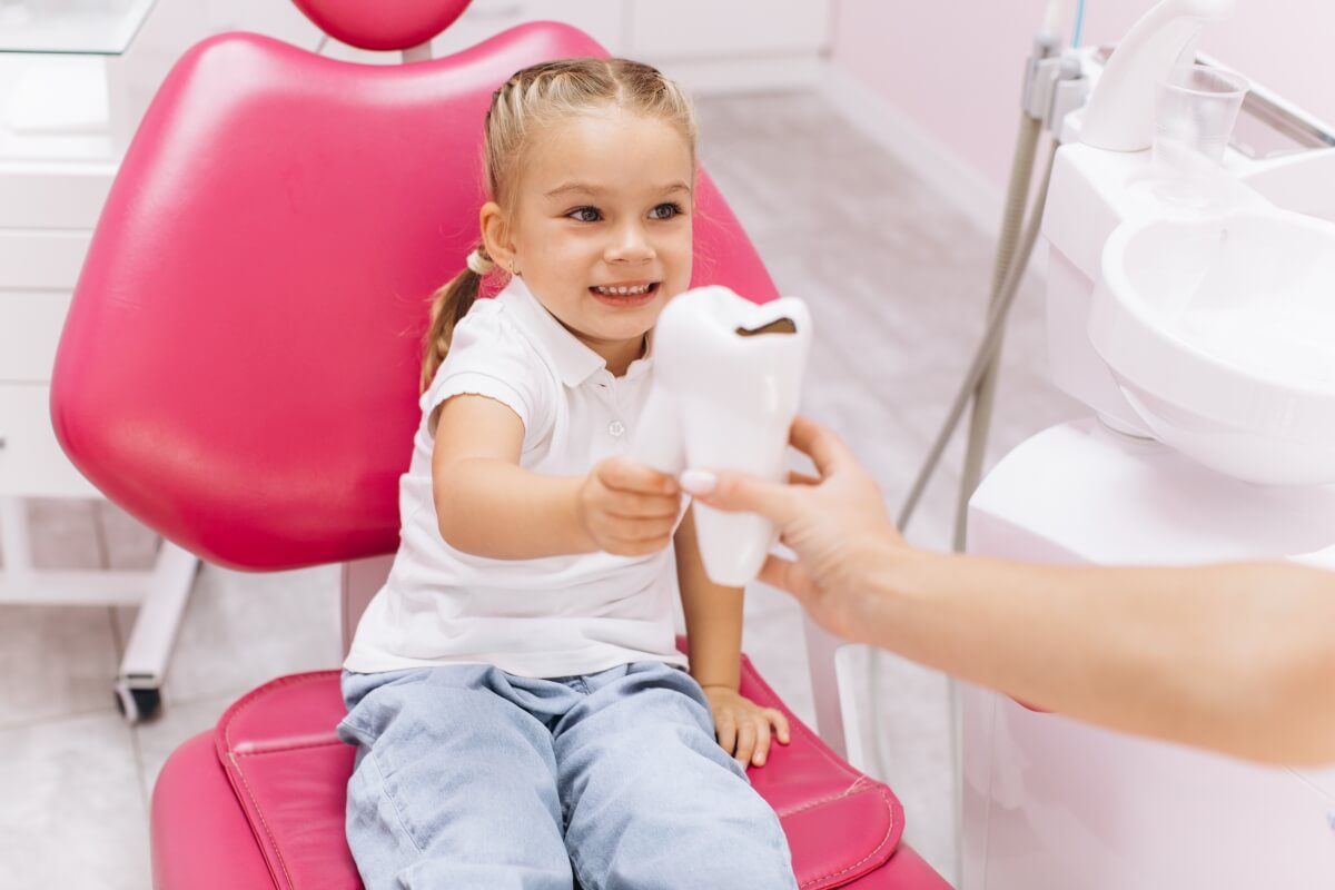 Dziewczynka siedzi na fotelu dentystycznym, a stomatolog leczenie wad wymowy wspiera uśmiechniętą pacjentkę.