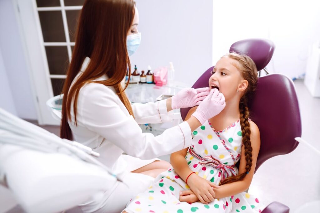 Dentystka bada zęby dziewczynki, obalając mity o stomatologii dziecięcej.