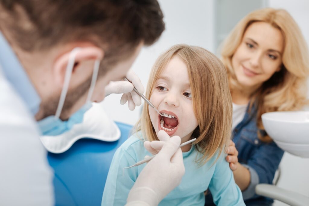 Dziecko na wizycie kontrolnej u dentysty, przypominające jak często odwiedzać stomatologa dziecięcego.